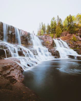 A wide shot of a multi-tiered waterfall spilling into a serene, clear pool.