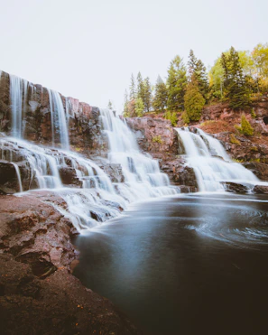 A wide shot of a multi-tiered waterfall spilling into a serene, clear pool.