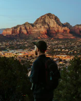 A traveler with a backpack looking at a city skyline during golden hour.