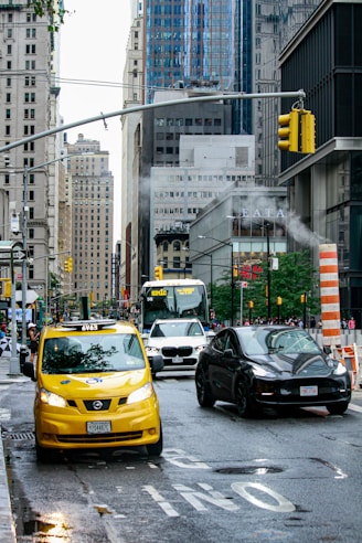 a yellow taxi cab driving down a street next to a black car