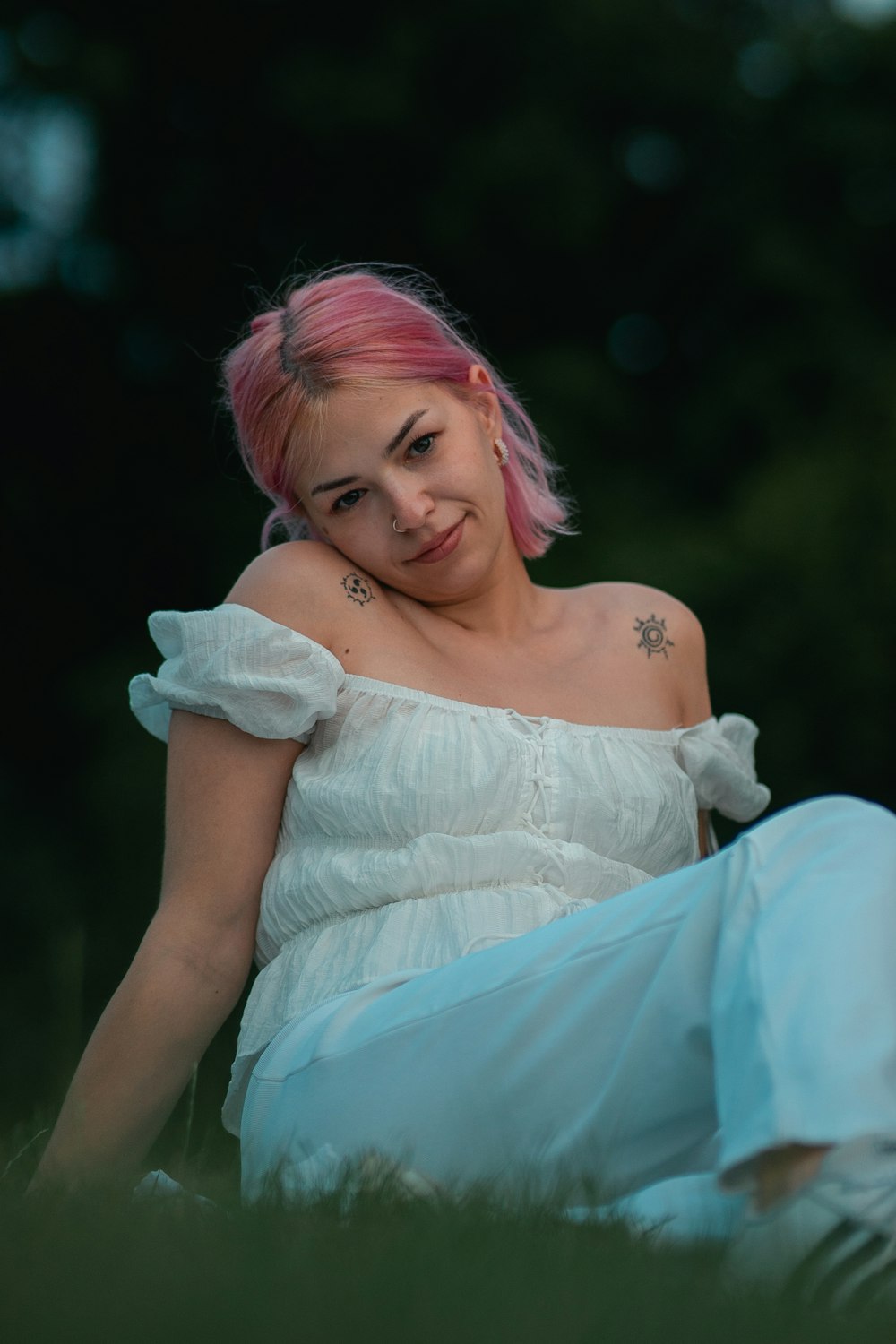 a woman with pink hair sitting in the grass