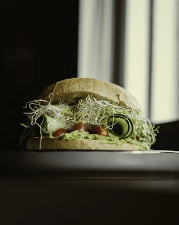 A smiling chef carefully assembling a sandwich with fresh, colorful ingredients.