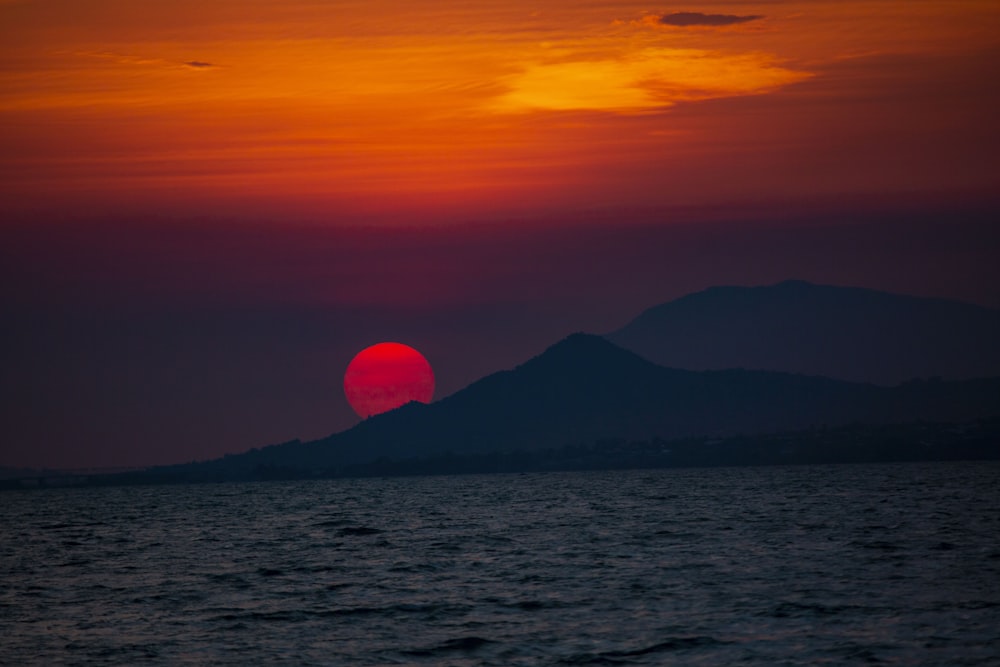 the sun is setting over the ocean with mountains in the background