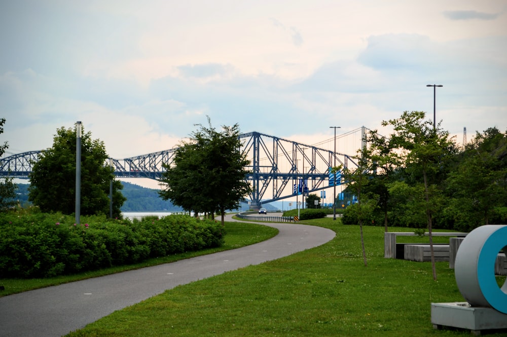 a large blue bridge over a river next to a lush green park
