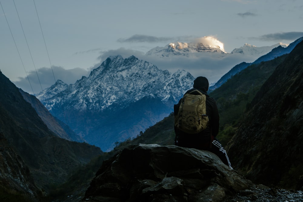 una persona seduta su una roccia che guarda le montagne