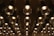 A ceiling installation composed of numerous circular, transparent glass light fixtures with metallic supports. The fixtures are arranged in a grid pattern, reflecting ambient light and casting soft glows. The reflection on the mirrored surface enhances the symmetrical appearance.