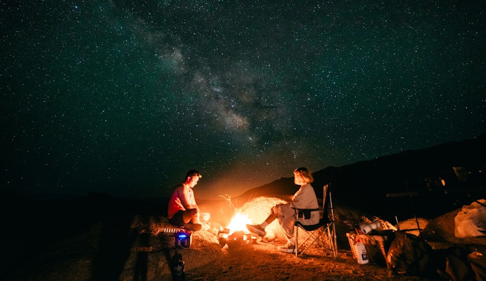 a group of people sitting around a campfire under a night sky filled with stars