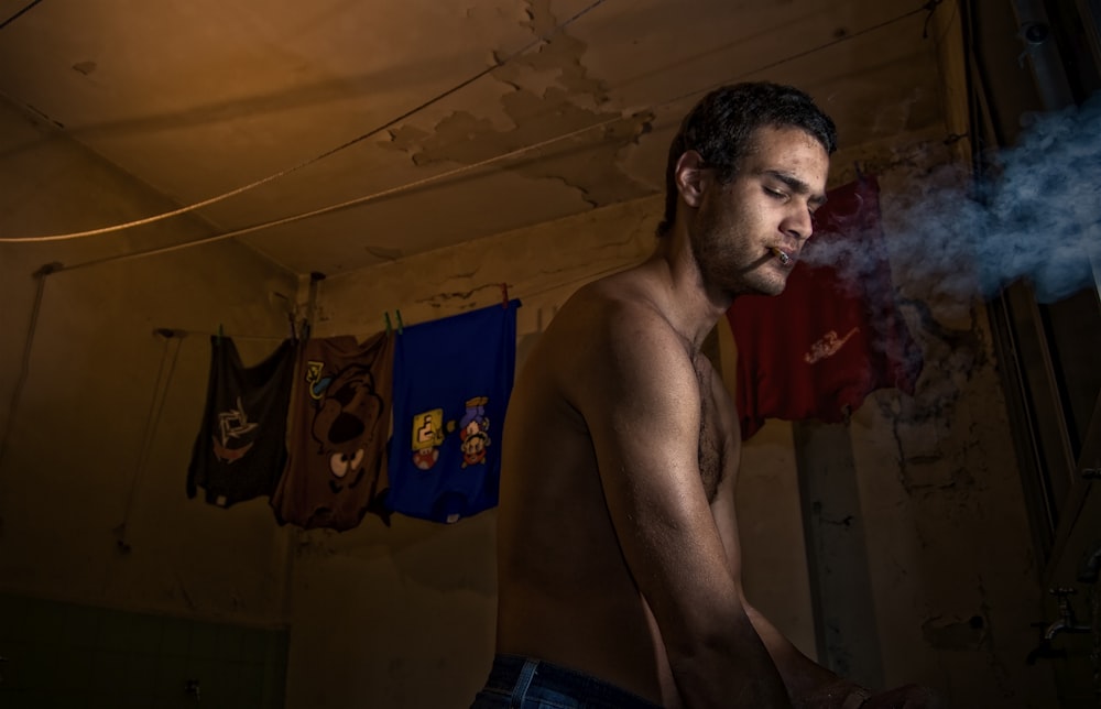 a shirtless man smoking a cigarette in a dark room