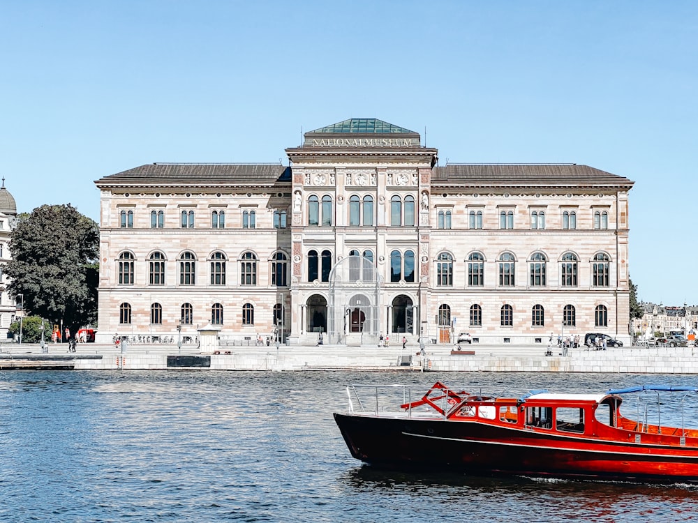 Um barco vermelho está na água em frente a um grande edifício