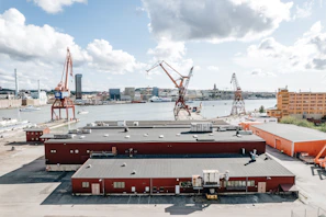 A panoramic view of a bustling industrial harbor with cranes and cargo vessels under a clear sky.