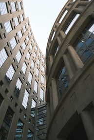 Two modern buildings with curved facades rise towards the sky, featuring numerous windows. The structures are made of concrete and glass, showcasing an architectural design that is both functional and aesthetically pleasing.