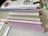 A collection of pastel-colored markers is arranged on a table alongside a notebook with decorative stickers and papers. The markers are mostly in soft shades of beige, pink, gray, and purple. Next to the markers, there is a visible edge of a calendar or workbook and some highlighter pens in a plastic case.