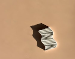 An elegant sculptural object in soft beige tones, casting gentle shadows on a textured concrete surface.