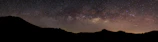 A panoramic view of the Milky Way arching over a quiet mountain range.