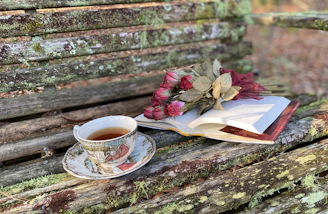 A stack of Susan’s books tied with a ribbon, placed beside a steaming cup of tea on a rustic wooden bench.