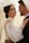 A couple embracing each other, with the woman smiling confidently while wearing an elegant white bridal gown adorned with pearls and a sheer veil. The man, dressed in a formal suit, looks lovingly at her, creating a romantic and intimate atmosphere.