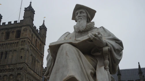 An aged statue of a revered scholar holding a tome, set against a dark library backdrop.