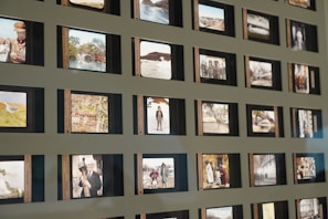 A collection of vintage slide photographs arranged in a grid pattern on a wall, each slide displaying various images such as people, landscapes, and buildings. The slides are bordered in black frames with some having handwritten labels.