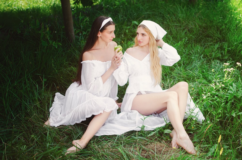 two women in white dresses sitting on the grass