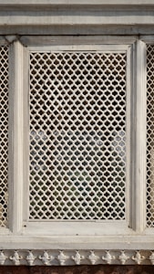 A detailed panel with intricate lattice work, featuring a symmetrical and repetitive geometric pattern set within a stone frame. The design suggests traditional craftsmanship and artistic heritage.