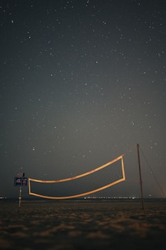 Evening volleyball practice under bright floodlights on a sandy court.