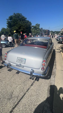 Crowd admiring a vintage car at an outdoor automobile show.
