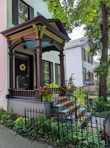 Inviting front porch of a light brown cottage surrounded by soft greenery and a welcoming pathway.