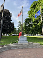 A wide shot of a peaceful memorial park with flags gently waving and visitors paying respects.