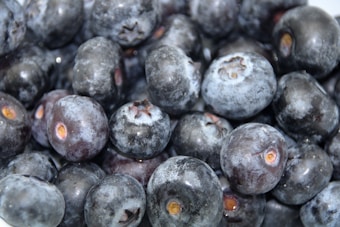 A close-up view of a pile of fresh, plump blueberries, covered with a layer of natural bloom, providing a slightly frosted appearance.