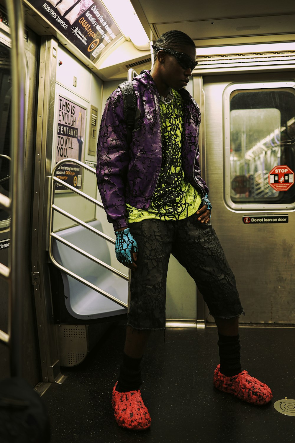 a man in a purple jacket and black pants standing on a subway