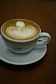 Artfully poured latte with intricate leaf design in a ceramic cup on a saucer.