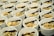 Multiple white bowls are arranged in rows, each containing a variety of food items. The contents include skewers with grilled meat, boiled eggs, and a mix of vegetables and herbs. Each bowl is served with a clear plastic fork.