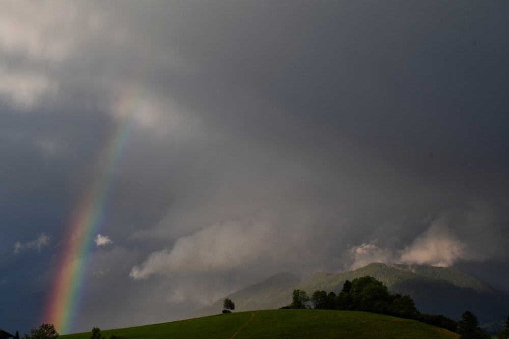 a rainbow in a cloudy sky over a green hill