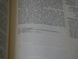 A close-up of an open book showing text in English, possibly a page from a religious or historical text, with two columns of text and footnotes at the bottom. The focus is on the left page.