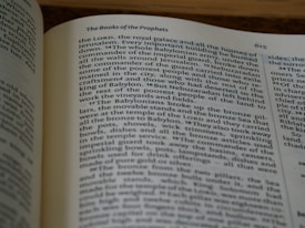A close-up view of an open book displaying text in a serif typeface. The text details historical or biblical content, mentioning figures like Nebuzaradan and cities such as Jerusalem. The page is numbered 615 and has a heading labeled 'The Books of the Prophets.' The lighting gives the page a warm tone with soft shadows, indicating a serene reading environment.