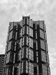 A high-rise building with a modern architectural design features a series of glass panes and sharp geometric shapes. The structure appears to have multiple protruding sections with reflective surfaces, creating a pattern of lines and angles.