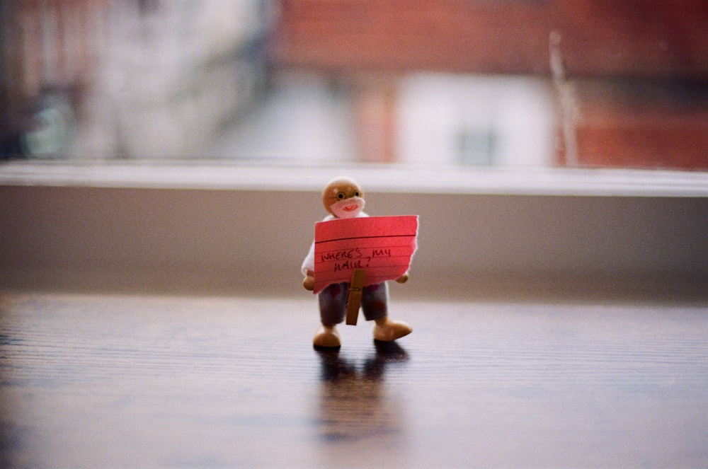a small figurine holding a red sign on top of a wooden table