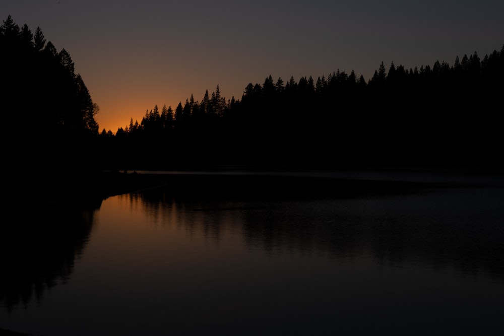 the sun is setting over a lake surrounded by trees