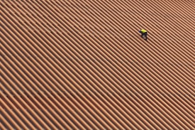 A person is wearing a yellow safety vest while working on a large, sloped roof made of brown and orange tiles in diagonal stripes.