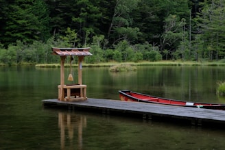 a red boat sitting on top of a lake next to a dock