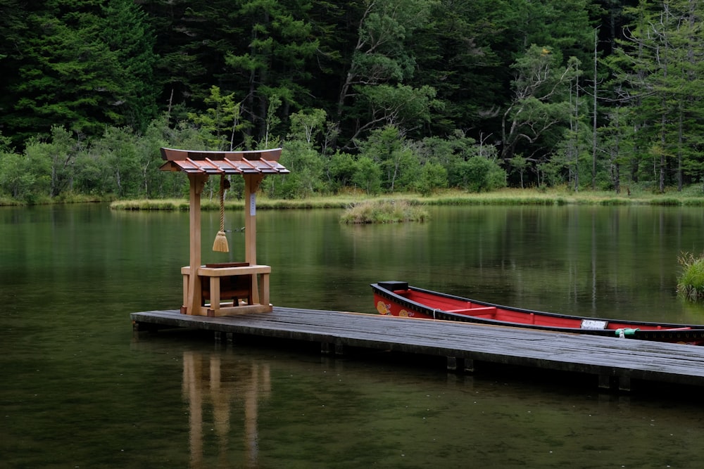 a red boat sitting on top of a lake next to a dock