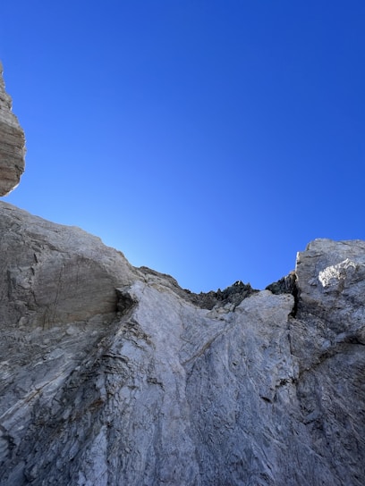A rugged rock face being carefully fragmented by specialized demolition equipment under a clear sky.