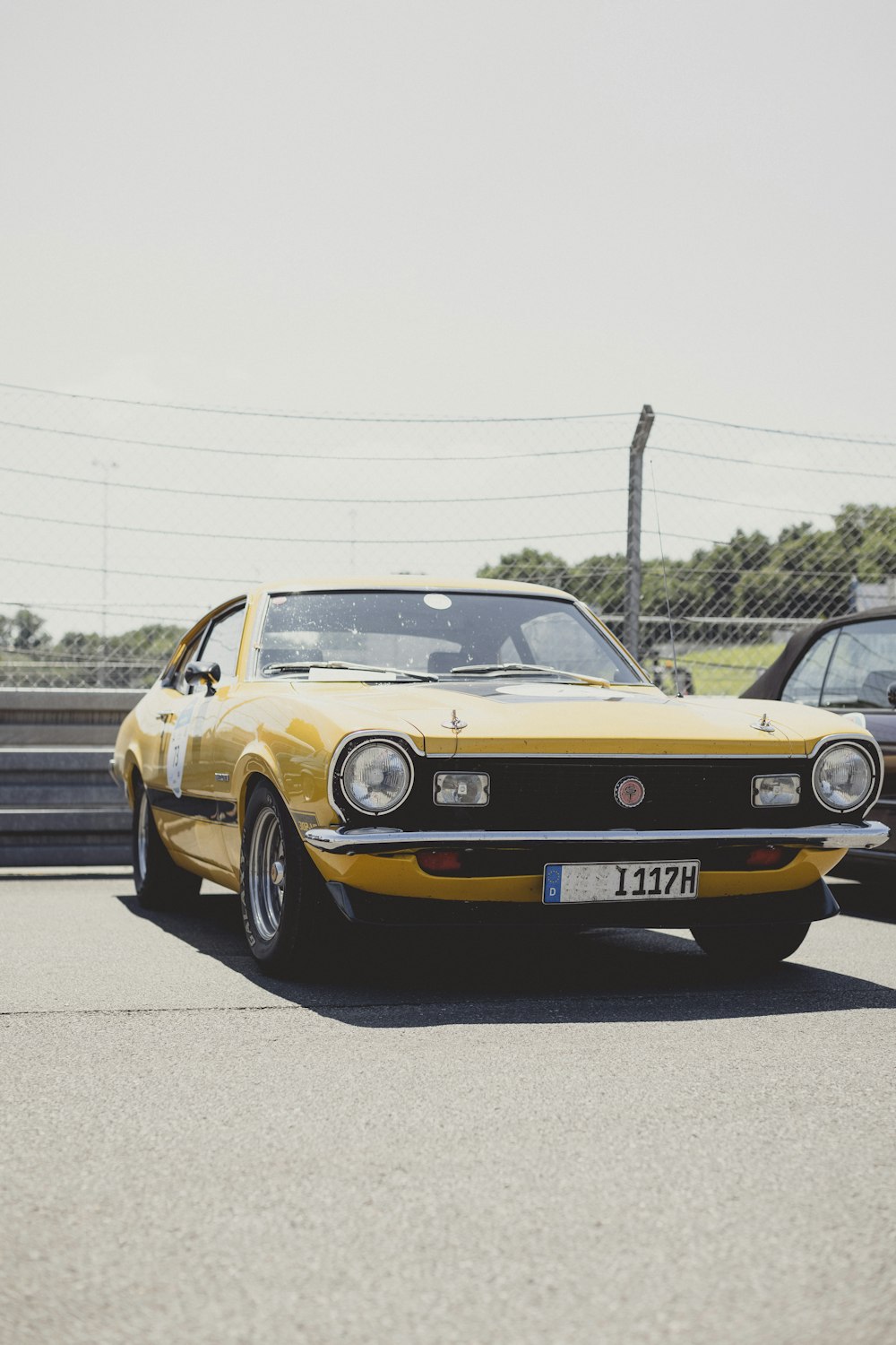 a yellow car driving down a road next to another car