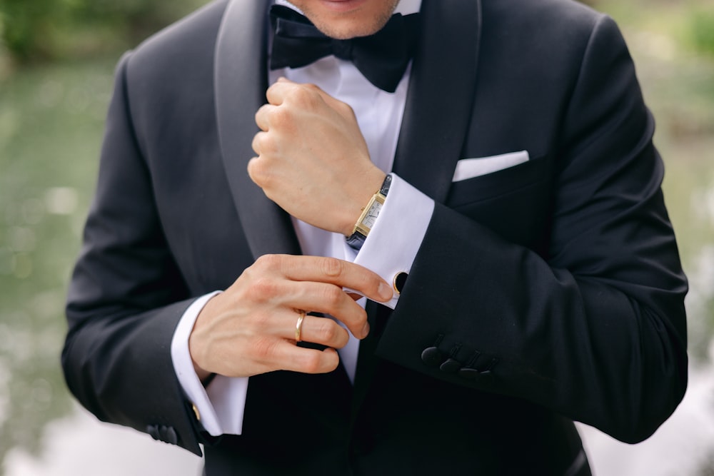 a man in a tuxedo adjusts his watch