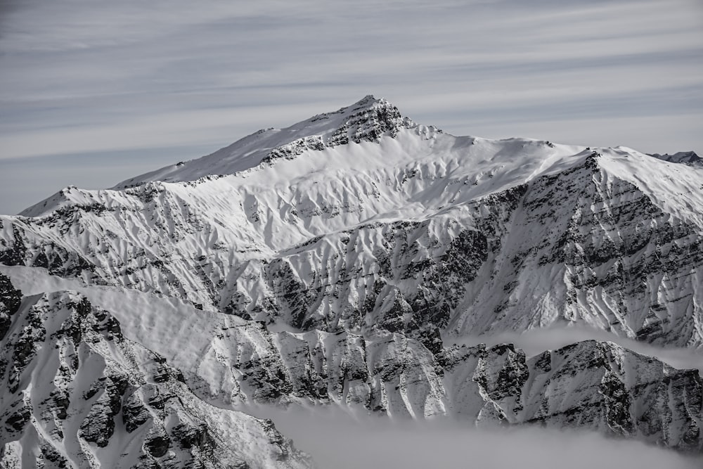 a mountain covered in snow and clouds under a blue sky