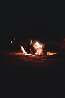 A cozy campfire glowing warmly in the twilight with rustic kitchen tools hanging nearby.