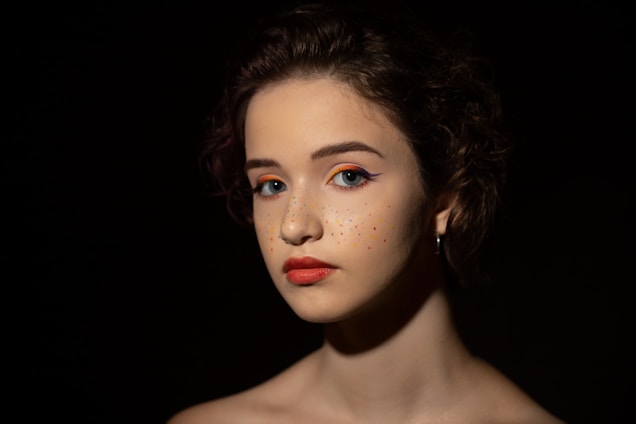 A vibrant young woman applying colorful makeup with confidence in a bright, cozy room.