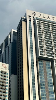 Tall modern skyscrapers with glass and metal facades dominate the scene. The architecture includes many windows and geometric lines, providing a contemporary urban feel. One of the buildings has a logo and partial word at the top.