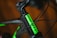 Close-up of a bicycle frame with rain droplets covering the surface. The frame features a prominent green logo against a black background, with cables running alongside.