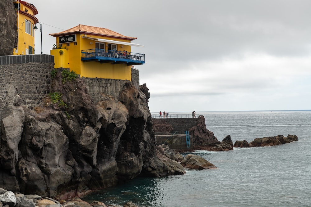 a yellow house sitting on top of a cliff next to the ocean